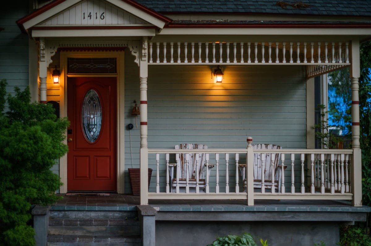 A porch with a red door, wooden armchairs and warm lights