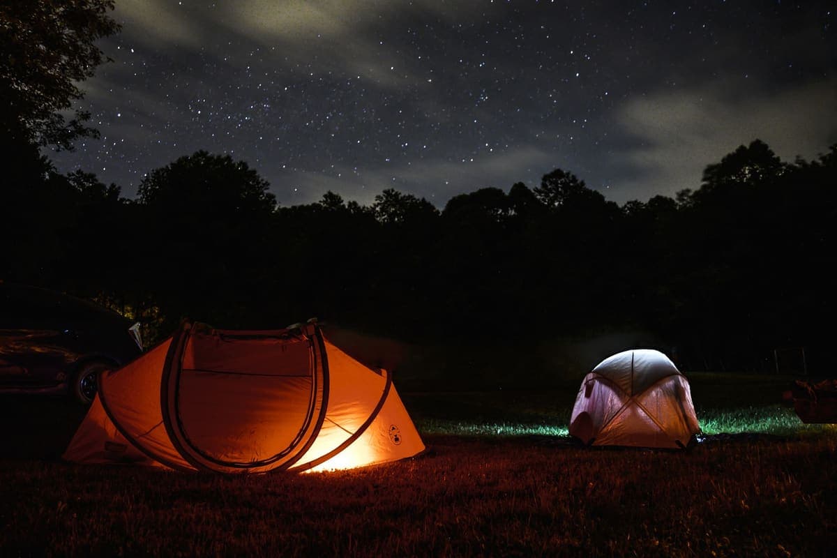 Glowing tents at a night camping scene under a starlit sky