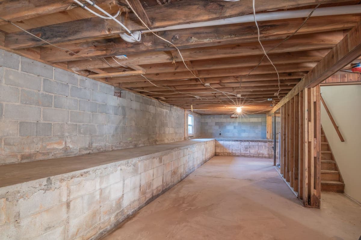 An empty basement with exposed wooden beams, concrete walls and a staircase