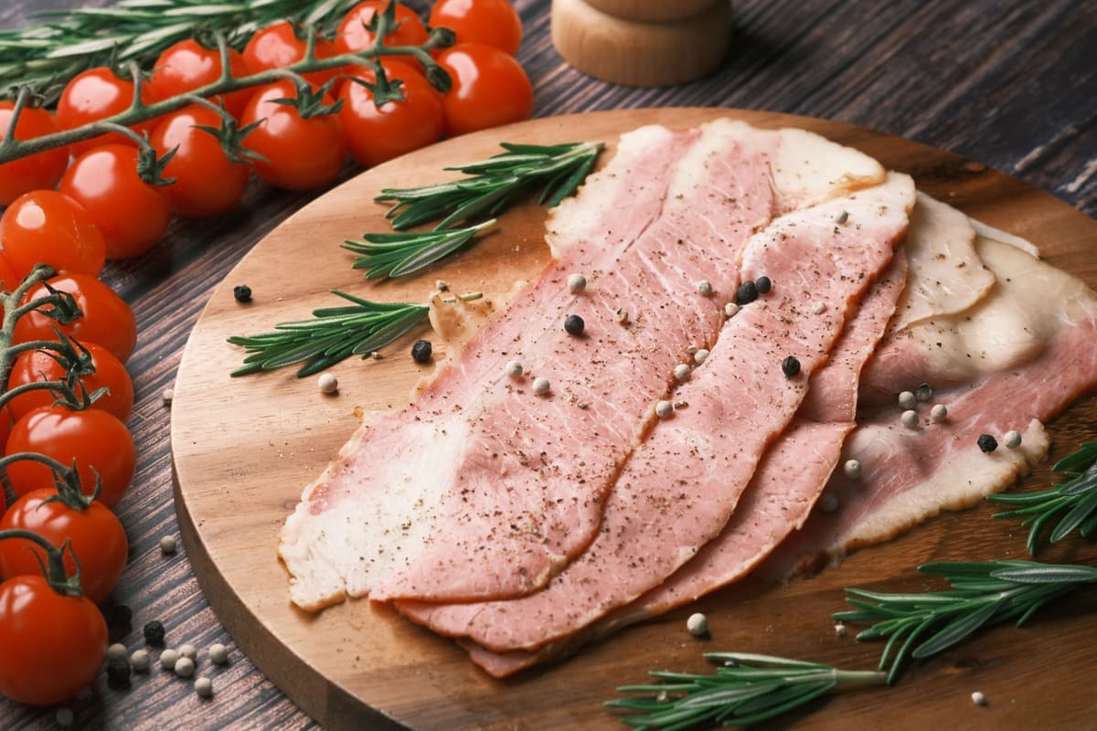 Cured meat slices with rosemary and tomatoes on a wooden board