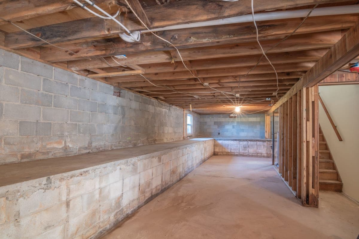 An empty basement with exposed wooden beams and concrete walls