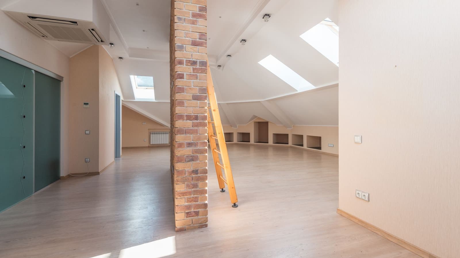 A spacious attic room lit by skylights with a brick pillar and wooden ladder