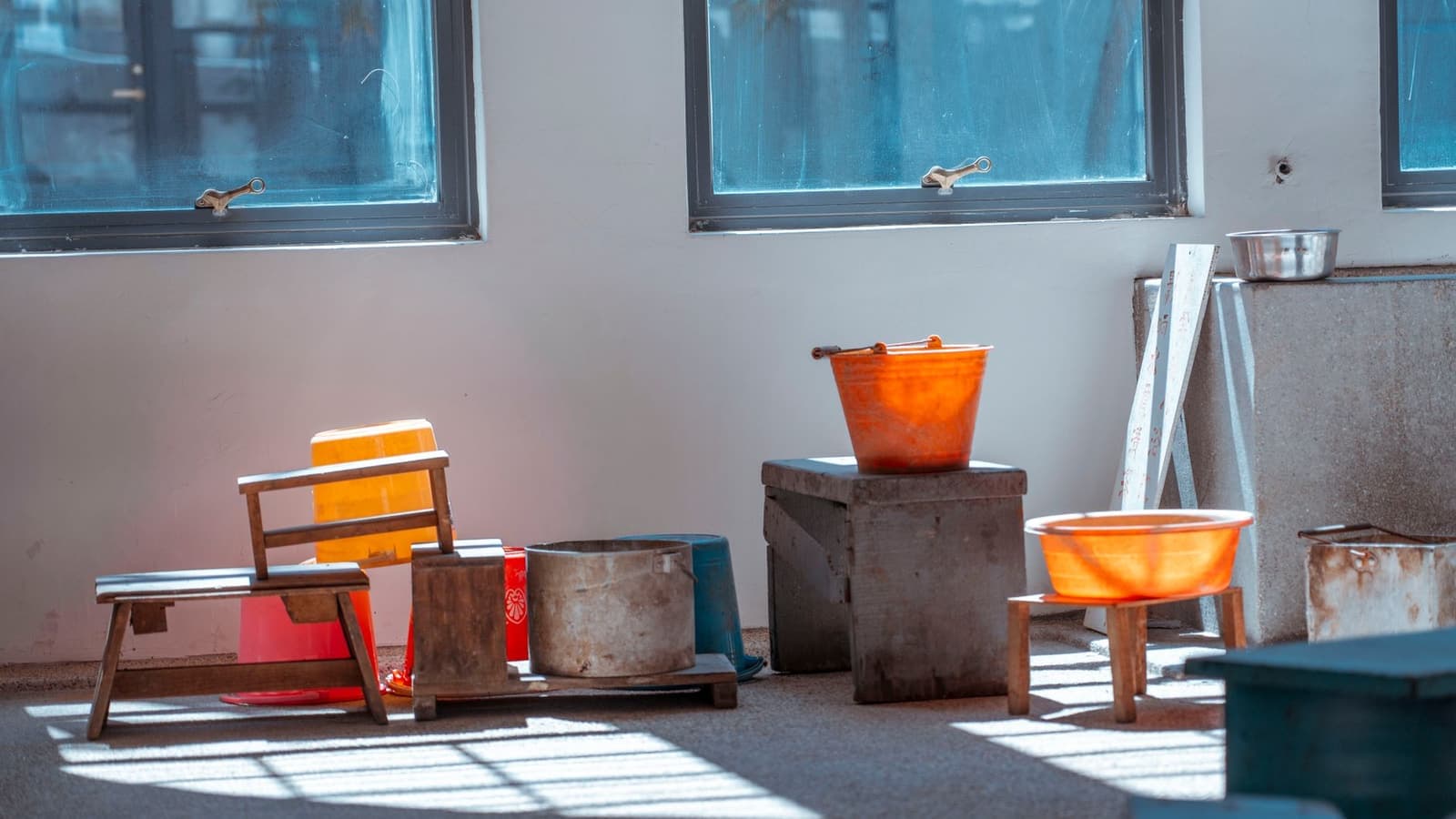 Plastic buckets and wooden stools in a rustic indoor setting