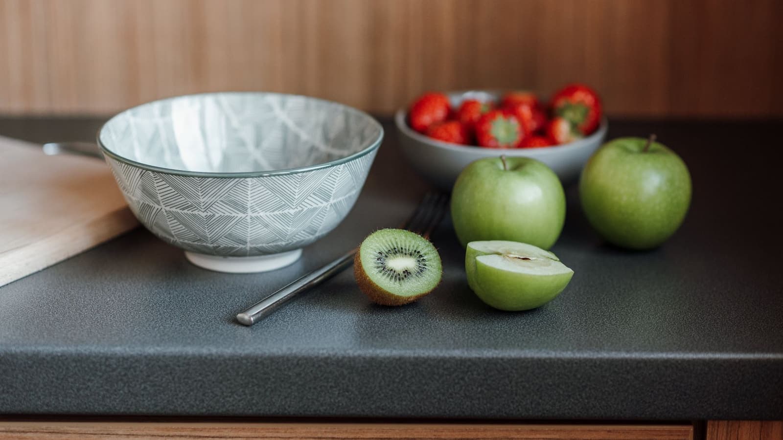 A light kitchen table with a bowl of apples, kiwi and strawberries