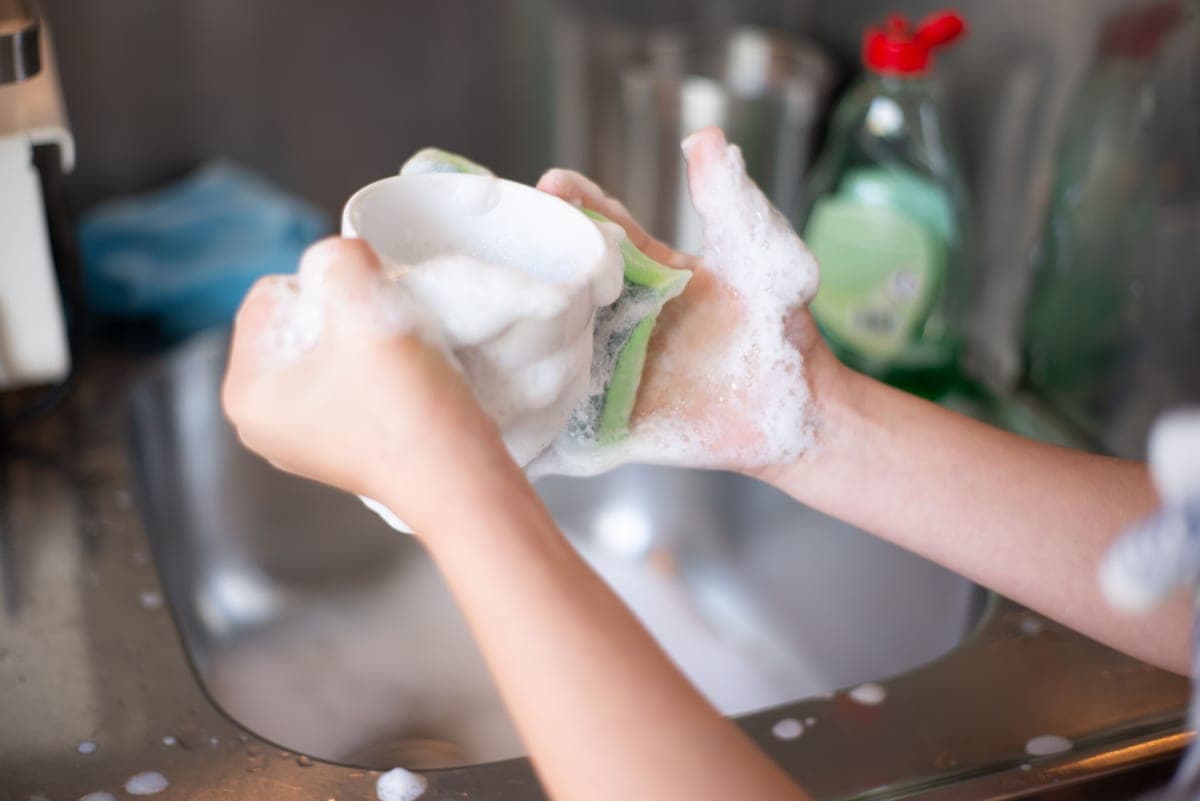 Hands washing a cup with soap suds in a kitchen sink