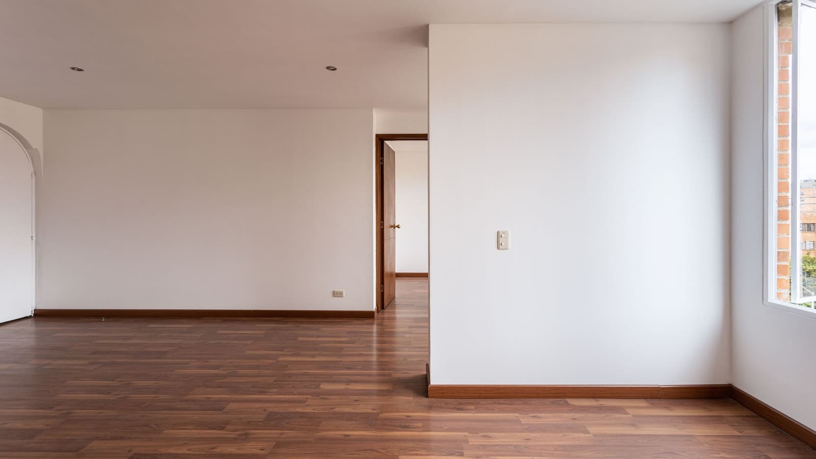 An empty room with bare wooden floors and white baseboards
