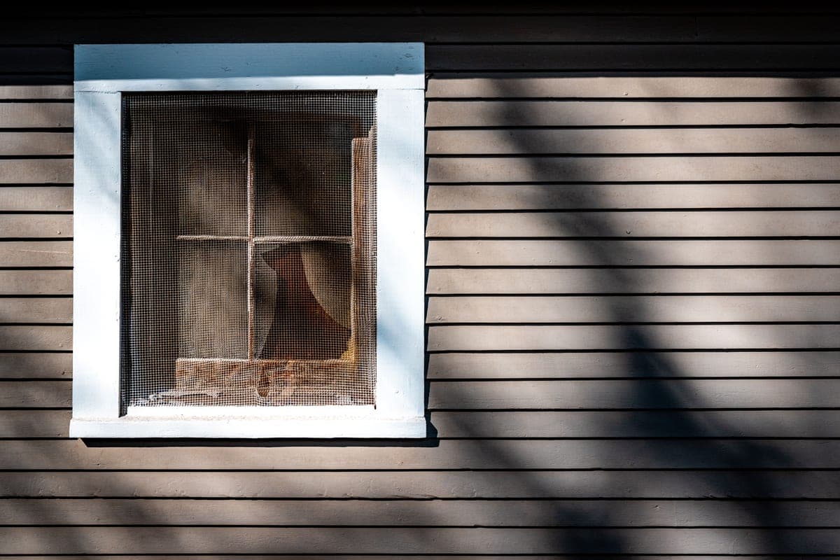 A rustic wooden house exterior with a window and insect screen