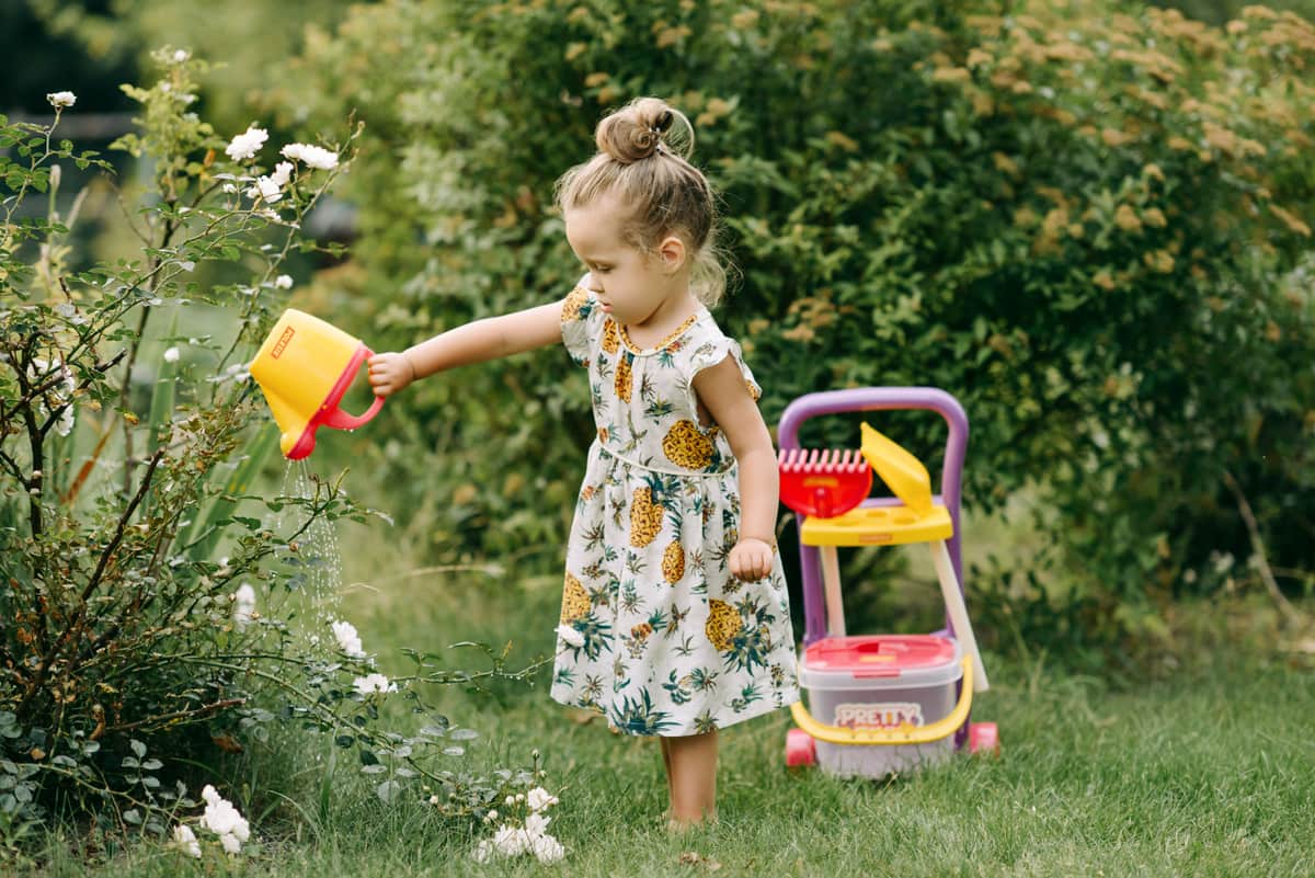 A young girl watering plants outdoors with a toy watering can
