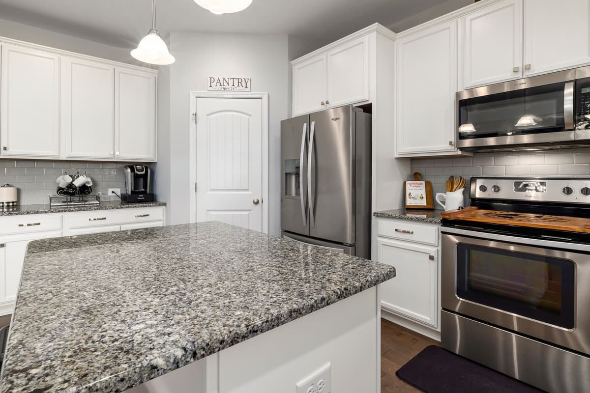 A kitchen with white cabinets, a pantry door, refrigerator and range
