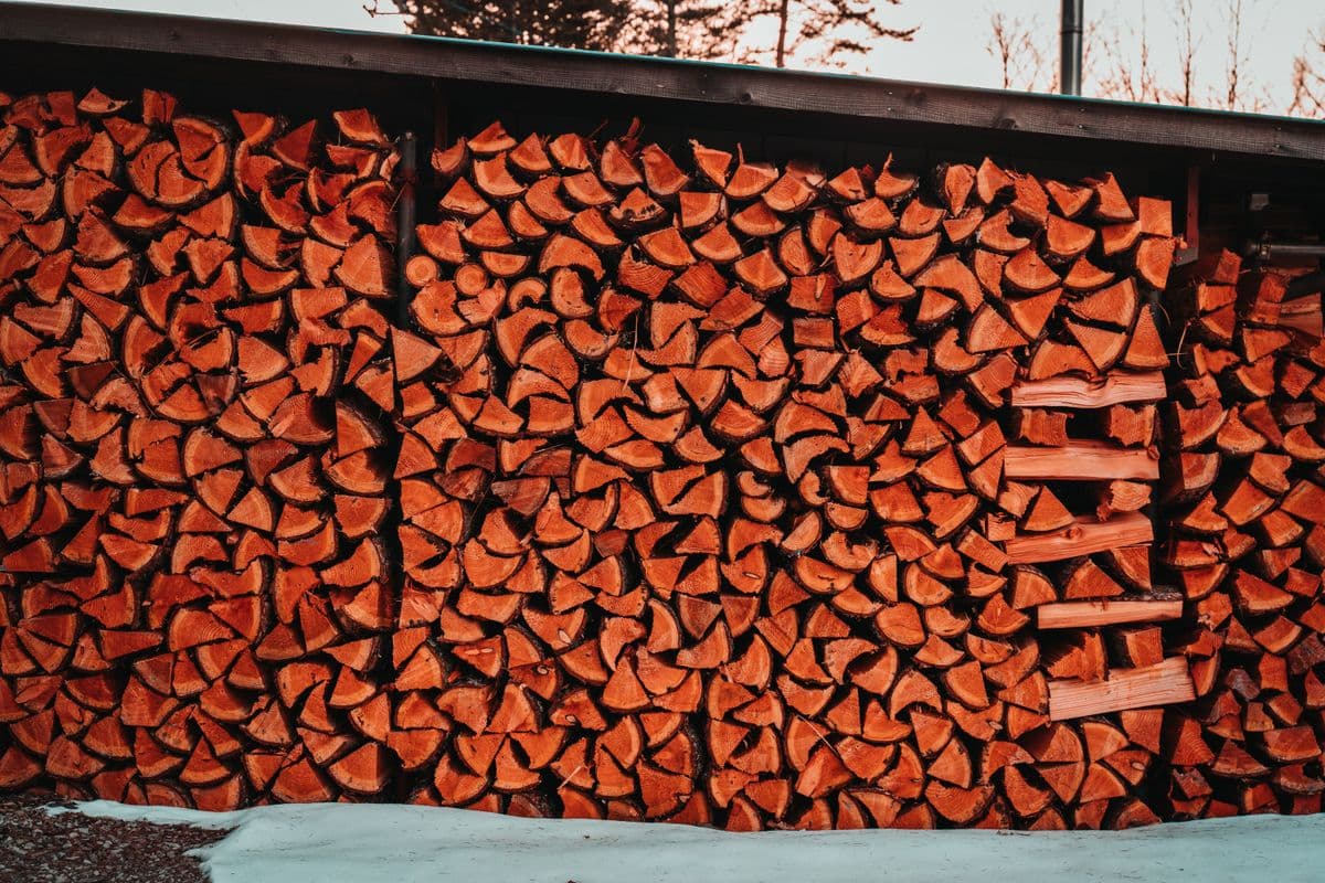 A large stack of chopped firewood stored outdoors beside a yard