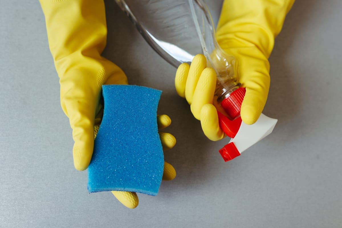 Hands in yellow gloves holding a sponge and a spray bottle