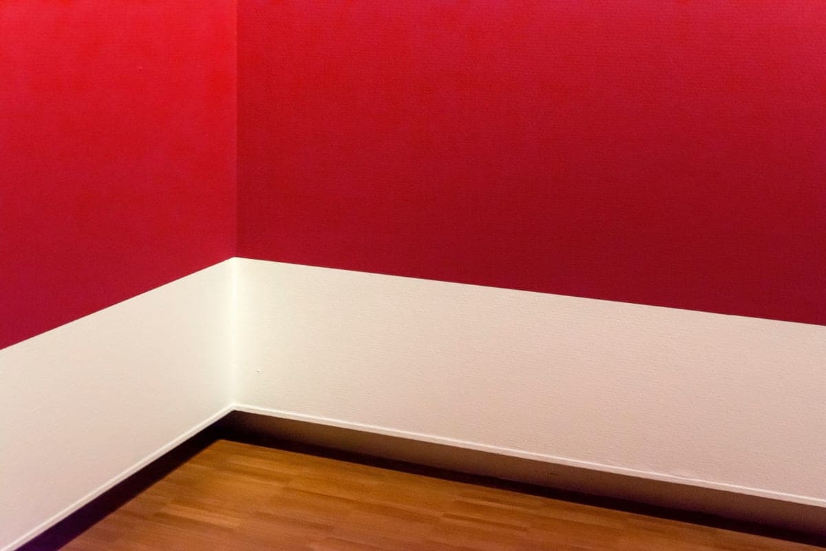 A minimalist room corner with red walls and wooden flooring