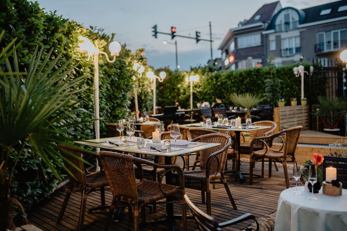 An outdoor restaurant terrace with empty tables and warm lighting at dusk