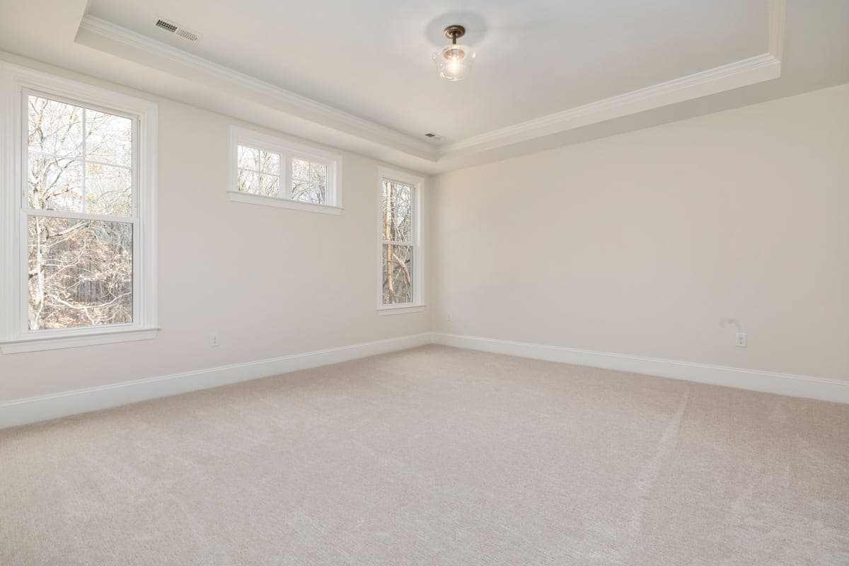 A bright empty room with large windows and carpet flooring