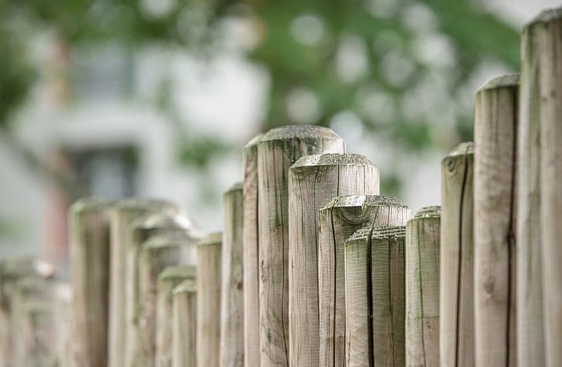 A weathered wooden fence post in close-up against a blurred garden