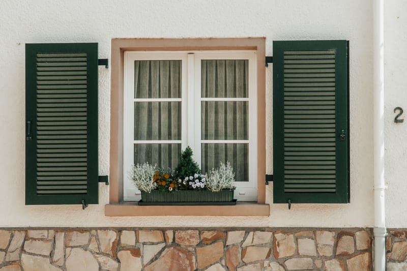 A house exterior with green shutters and a planter beneath the window