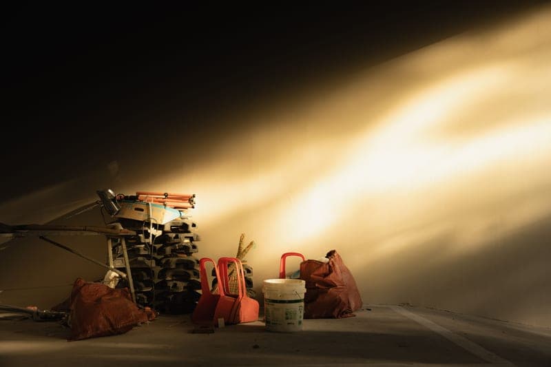 A sunlit garage corner with tools and chairs stacked against the wall