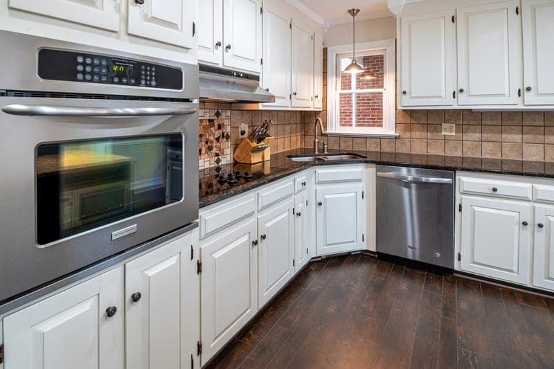 A kitchen with white cabinets, steel appliances and a wooden floor
