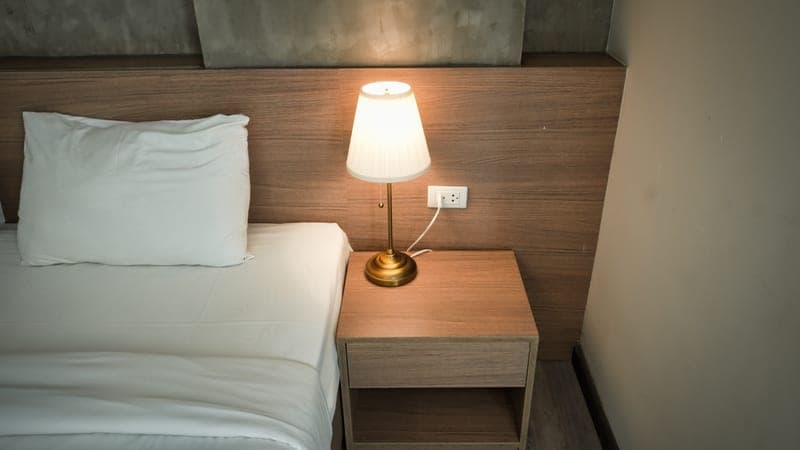 A bedroom nightstand with a lamp switched on