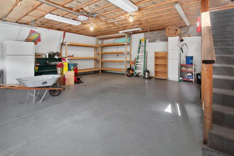 A garage with storage shelving, hand tools and a wheelbarrow
